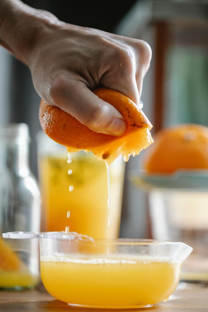 Crop faceless person squeezing ripe orange while making fresh juice in kitchen at home